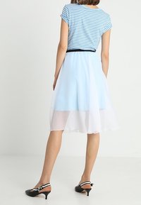 Vaaleansininen raidallinen toppi, jossa on käännetyt hihat, yhdistettynä kerrostettuun vaaleansiniseen ja valkoiseen läpikuultavaan hameeseen. Mustat korot, joissa on valkoisia ja mustia yksityiskohtia.