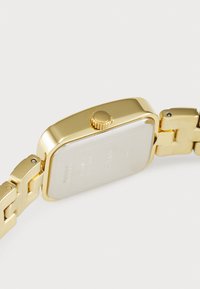 Gold rectangular watch with a polished surface, featuring a crown on the side and a linked band. The back is smooth with engraved text.