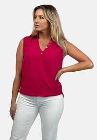 Fuksjowa bezrękawnikowa bluzka o kroju kopertowym, z guzikami i teksturowanym materiałem; w zestawie z białymi spodniami.