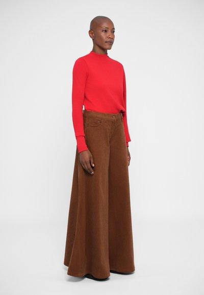 Top rojo de manga larga combinado con pantalones de pana marrones de pierna ancha. El conjunto presenta un diseño ajustado y una tela texturizada, enfatizando la forma y el color.