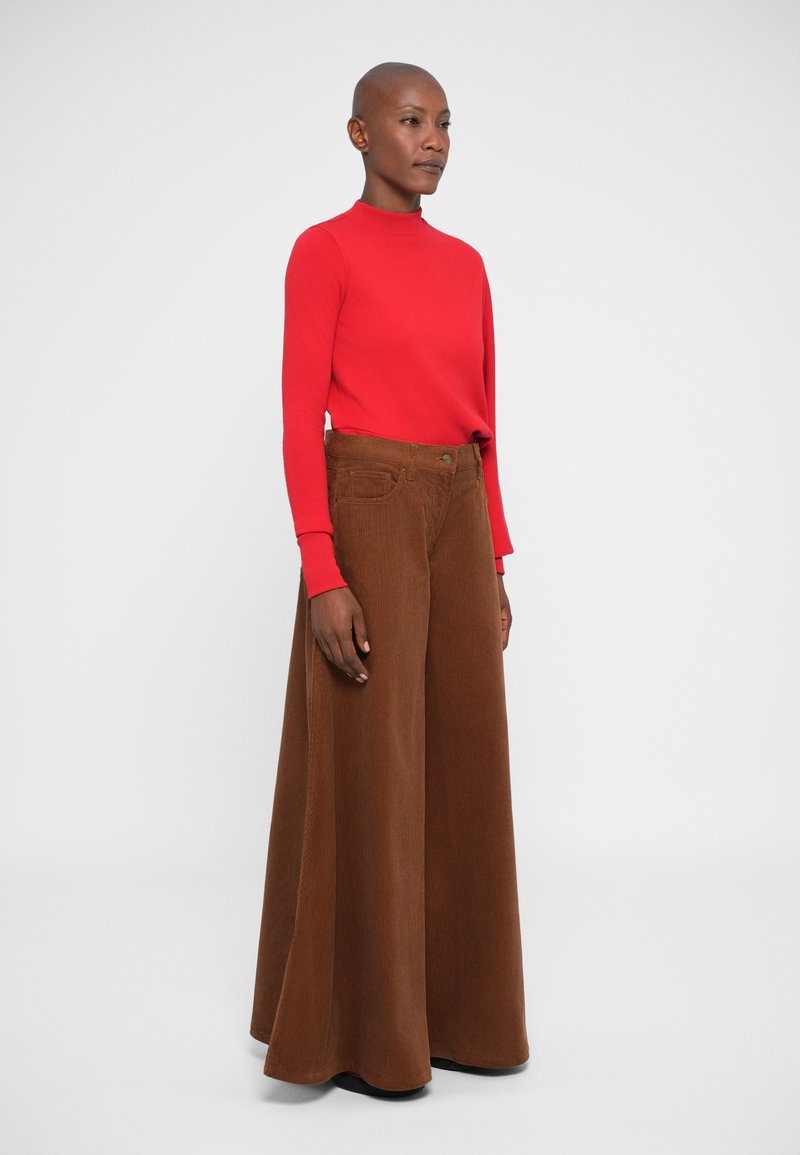 Red long-sleeve top paired with wide-leg, brown corduroy pants. The outfit features a fitted design and textured fabric, emphasizing shape and color.