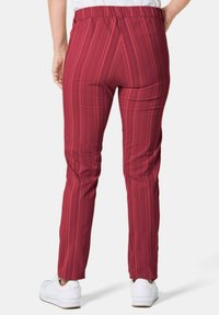Rood gestreepte broek met een elastische tailleband en smalle pijpen, gecombineerd met witte sneakers. Het materiaal lijkt glad met een subtiele glans.