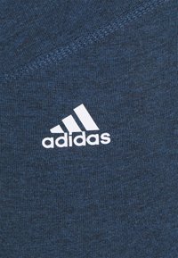 Tmavě modré sportovní tričko se strukturovanou tkaninou, se zvýrazněným bílým logem Adidas v dolním levém rohu.