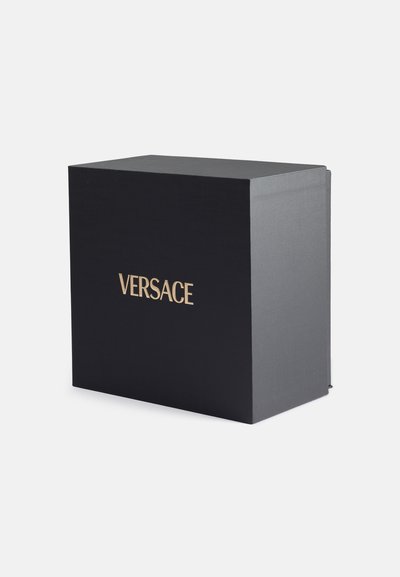 Melna dāvanu kaste ar teksturētu apdari, priekšpusē ar zeltītu tekstu "VERSACE". Kvadrātveida forma ar vāku un bez redzamām detaļām.