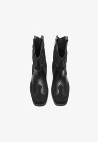 Botines negros que presentan una combinación de cuero liso y ante, con intrincados bordados en los lados y un diseño curvado distintivo.