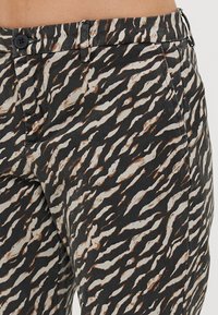 Pantaloni neri e crema con motivo a onde, design astratto con accenti ruggine. Comprendono una chiusura con bottone e tasche laterali.