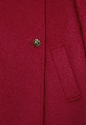 Punane villane mantel tekstureeritud pinnaga, millel on kuldne nööp ja küljetasku. Kanga välimus on soe ja pehme.