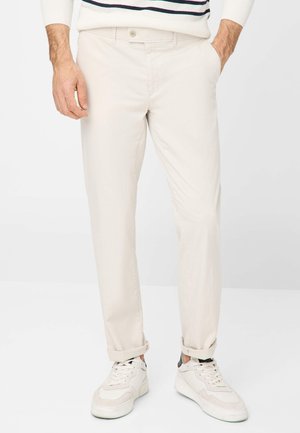 Beige chinos featuring a straight-leg design and rolled cuffs, paired with white sneakers. Cotton fabric with a smooth texture.