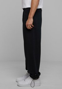 Sorte sweatpants med en afslappet pasform, elastisk talje og snor. Båret med hvide sneakers, der har en glat stofstruktur.