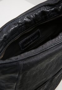 Czarna skórzana torba z teksturowanym wykończeniem, zamykana na zamek, o miękkim wnętrzu. Posiada małą metkę wewnątrz, pokazującą szczegóły rzemiosła.