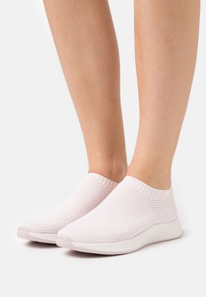 Füße in hellrosa, zum Hineinschlüpfen geeigneten, gestrickten Mesh-Sneakern mit weißen Sohlen vor einem schlichten weißen Hintergrund.