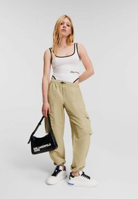 Vit linne med svart kant och logotyp, tan cargo-byxor med sidofickor, svart handväska och vita sneakers med svarta detaljer.