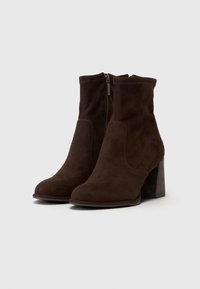 Bottes de cheville en daim marron avec un talon bloc haut, fermeture éclair sur le côté et finition lisse ; elles présentent des détails cousus et un bout arrondi.