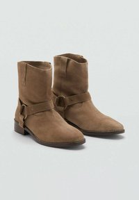 Botas de tobillo de ante marrón con diseño de punta afilada, que cuentan con una correa lateral con hebilla y un bajo tacón de madera.