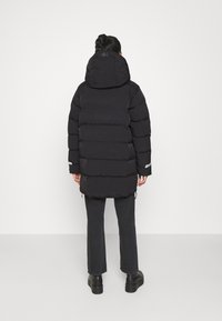 Chaqueta de plumas negra con capucha desmontable, diseño acolchado y puños elásticos. Combinada con jeans oscuros y botas negras gruesas.