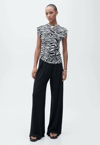 Mouwloze top met zebra-patroon en een gedrapeerd ontwerp, gecombineerd met losse zwarte broeken met een gladde textuur en wijde pijpen.