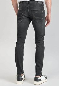 Jeans de mezclilla negros ajustados con detalles desgastados, dos bolsillos traseros y dobladillos deshilachados, combinados con zapatillas blancas con acentos negros.