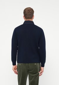 Marineblauwe pullover met een opstaande kraag, gemaakt van zachte stof. Lange mouwen en een getailleerd design passen mooi bij olijfgroene corduroy broek.