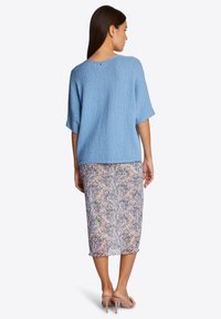 Helles blaues, strukturiertes Strickoberteil mit kurzen Ärmeln und einem Knopfdetail am Rücken, kombiniert mit einem floralen, transparenten Midirock.