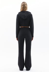 Geknipte hoodie en uitlopende broek in donkergrijze stof. De hoodie heeft een capuchon en lange mouwen; de broek heeft een aansluitende taille en wijde pijpen.