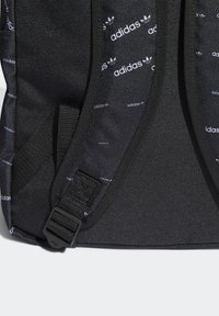 Svarta Adidas ryggsäcksspänen med upprepat vitt Adidas-logomönster och justerbar spännare på texturerad tyg.