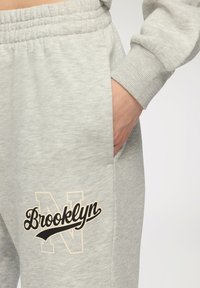 Szare dresowe spodnie wykonane z miękkiego materiału, z czarnym logo Brooklyn z stylizowanym „N” oraz boczną kieszenią do przechowywania.
