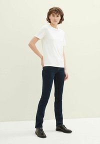 T-shirt blanc à manches courtes associé à un jean slim bleu foncé et des chaussures noires à lacets. Tissu lisse, design simple et coupe classique.