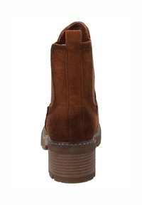 Botte cheville en suède marron avec un talon empilé, des panneaux élastiques sur les côtés et une languette à l'arrière. Semelle en caoutchouc texturé avec un motif de sculpture subtil.