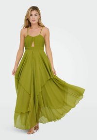 Zelené maxi šaty z chiffon s plisovaným korzetem, detaily ve tvaru klíče, tenkými ramínky, vrstvenou sukní a zvlněnými okraji. Nosené s nude podpatky.