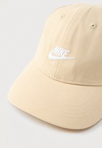 Beige Nike baseball sapka fehér hímzett logóval és több sor varrással a gömbölyített karimán.