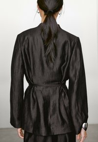 Schwarze, strukturierte Blazer mit langen Ärmeln, tailliertem Bund und lockerer Passform. Verfügt über einen glatten Stoff und ein minimalistisches Design.