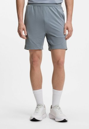 Mand iført grå træningsshorts, hvide crew-sokker og hvide sneakers stående mod en hvid baggrund.