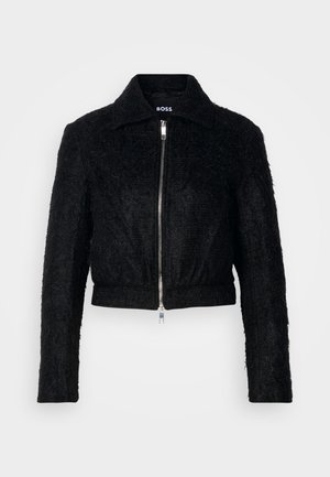 Schwarze, cropped Jacke aus strukturiertem Stoff mit einem Frontreißverschluss, spitzem Kragen und langen Ärmeln. Sie verfügt über ein glattes Futter und einen subtilen Glanz.