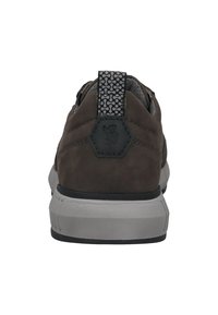 Dunkelbrauner Sneaker mit dicker weißer Sohle, gemustertem schwarzen und grauem Fersen-Zugband sowie einem aufgenähten sechseckigen Logo-Patch auf der Rückseite.