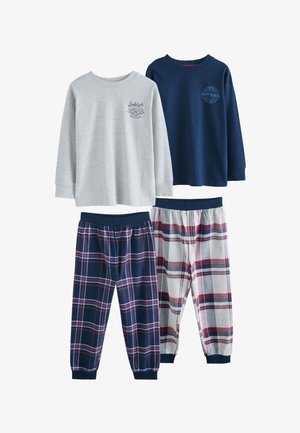 Due ragazzi con pantaloni da pigiama a quadri e maglie a maniche lunghe stanno in soggiorno, uno a piedi nudi, l’altro con pantofole blu navy.