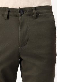 Pantalons vert olive en tissu texturé, avec une fermeture à boutons et des poches latérales. Design ajusté avec passants de ceinture et finition lisse.