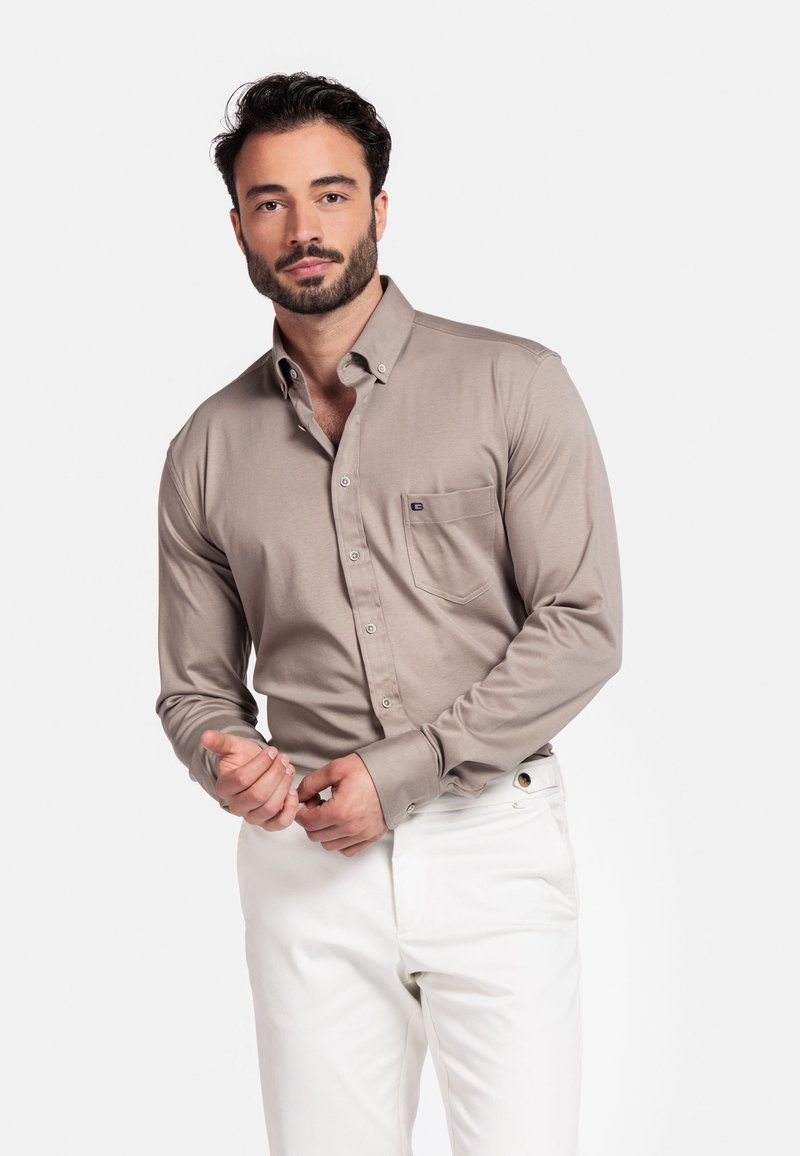  Lichtbeige overhemd met lange mouwen, knopen, een borstzak en een zachte textuur, gecombineerd met witte broek, gedragen door een model met donker haar.