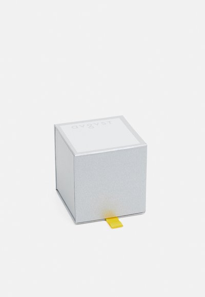 Srebrny kwadratowy box o błyszczącej powierzchni, z białą górą i żółtą tasiemką do ciągnięcia. Prosty design z tłoczonym napisem na wieczku.