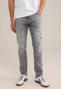 Jeans de mezclilla gris con un ajuste slim, que presentan un lavado desgastado, bolsillos clásicos y piernas ligeramente ajustadas, combinados con zapatillas blancas de corte bajo.