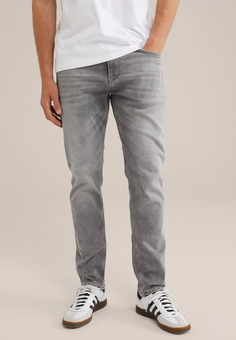 Jeans de mezclilla gris con un ajuste slim, que presentan un lavado desgastado, bolsillos clásicos y piernas ligeramente ajustadas, combinados con zapatillas blancas de corte bajo.