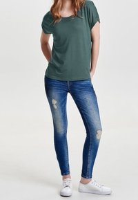 Green short-sleeve t-shirt with a rounded neckline, paired with blue skinny jeans featuring distressed details and white sneakers.