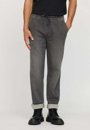 Jogging en denim gris avec taille élastique et cordon de serrage, présentant des ourlets roulés et une coupe décontractée. Associés à des bottes noires à lacets.