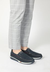 Mørkeblå loafers i blødt ruskind, med elastiske sideaccentuer, hvid gummisål og røde syninger, parret med grå ternede bukser.