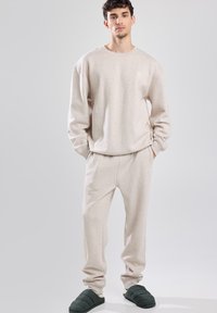 Felpa beige e pantaloni della tuta abbinati in tessuto morbido, con collo a giro e polsini elastici. Calzature verdi slip-on completano l'outfit.