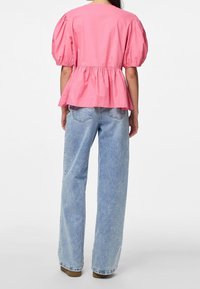 Blusa rosa con mangas abullonadas y dobladillo peplum, hecha de una tela liviana. Combinada con jeans de pierna ancha de color azul claro, mostrando una vista trasera informal.
