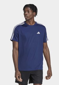 T-shirt de sport bleu marine en tissu léger, avec des accents blancs à trois bandes sur les épaules et un petit logo de marque blanc sur la poitrine.
