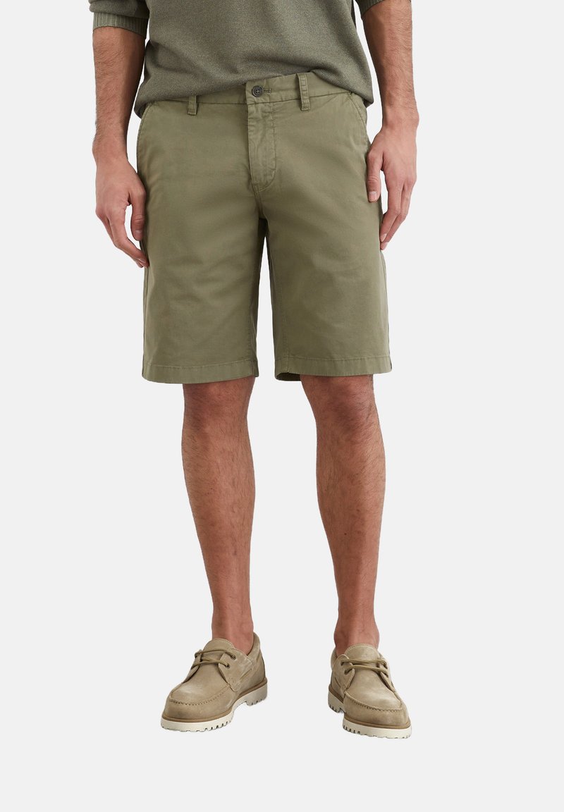 Shorts en coton vert olive avec devant plat, poches latérales et passants de ceinture. Portés avec des chaussures en daim beige clair.