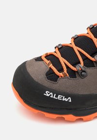 Scarpa da trekking grigia e nera con lacci arancioni, dotata di una tomaia testurizzata, suola in gomma e logo del marchio visibile.