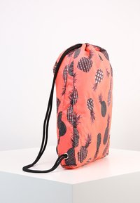 Sac à cordon corail avec motif d'ananas noir, fabriqué en tissu léger, doté de bretelles réglables et d'une texture lisse.