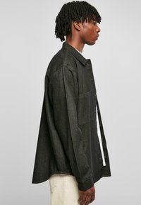 Camicia in denim nero con chiusura a bottoni frontale, maniche lunghe e taschino sul petto. Presenta una vestibilità rilassata e un motivo testurizzato sottile.